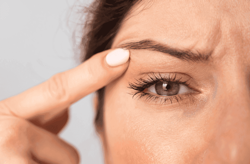 Close-up of a person touching their eyebrows with a finger, showing a focused expression.